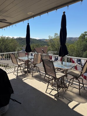 An outdoor patio with a table and chairs, umbrellas, and a view of a hilly landscape. - 

Make yourself at home at this cozy and inviting lake house in Oak Shores (Bradley)