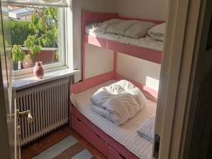 Ein Zimmer mit Etagenbetten, einem Fenster mit Blick auf Grünflächen, einem Heizkörper und einem Blumentopf.