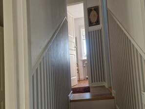 Eine Treppe mit gestreiften Wänden, einem Holzboden und einer Tür am oberen Ende, die in einen Raum mit einem Fenster führt.