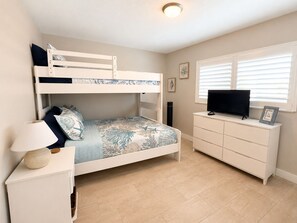 Ein Etagenbett mit Fernseher und Kommode, eine Lampe und ein Fenster mit Jalousien.