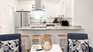 Eine moderne Küche mit weißen Schränken, einem Edelstahlkühlschrank und einer integrierten Kochinsel mit Spüle.