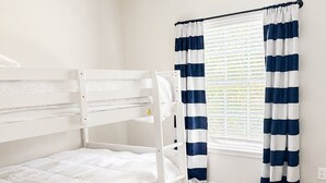 Ein Stockbett in einem Zimmer mit Deckenventilator, Holzboden und einem Fenster mit Streifenstoren.