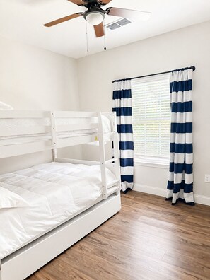 Ein Stockbett in einem Zimmer mit Deckenventilator, Holzboden und einem Fenster mit Streifenstoren.
