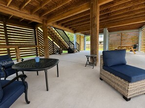 Ein überdachter Außenbereich mit einer Terrasse, einem runden Tisch, zwei Sofas, einem kleinen Tisch und einer Treppe zu einer erhöhten Ebene.