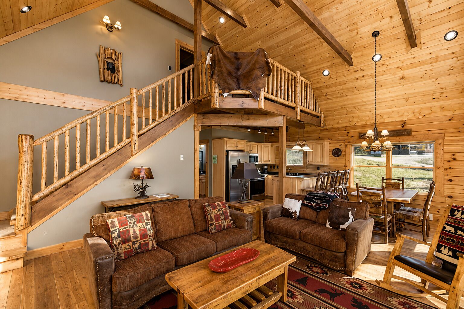 A rustic cabin interior with a wooden staircase, a dining area, and a kitchen.
