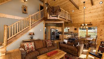 A rustic cabin interior with a wooden staircase, a dining area, and a kitchen.