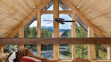 A wooden interior with large windows, a ceiling fan, and a view of a mountain landscape.