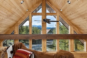 A wooden interior with large windows, a ceiling fan, and a view of a mountain landscape. - Mountain View Lodge+WiFi+AC+7MilestoYNP (West Yellowstone)