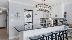 Une cuisine moderne dotée d’un îlot central, de tabourets de bar, d’un lave-linge et d’un luminaire suspendu.