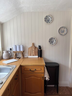 A kitchen with a wooden countertop, a sink, a kettle, a cutting board, and three decorative plates on the wall.