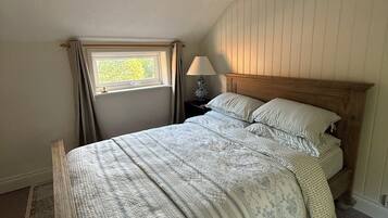 A bedroom with a wooden bed, a nightstand, a lamp, a window with curtains, and a ceiling fan.