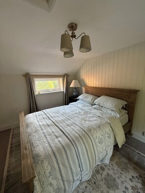 A bedroom with a wooden bed, a nightstand, a lamp, a window with curtains, and a ceiling fan. - Cottage 10 minutes away from beaches (Carlton road)