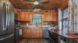 Uma cozinha com armários de madeira, eletrodomésticos de aço inoxidável, uma janela com persianas e um ventilador de teto.