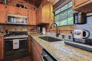 A kitchen with wooden cabinets, stainless steel appliances, granite countertops, and a window with a view of trees. - A View For Two | Ellijay, GA (Gilmer County)