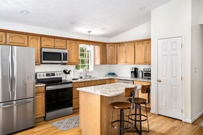 A modern kitchen with wooden cabinets, stainless steel appliances, a granite countertop, and a bar stool. - Basye Bungalow | Spacious 4BR/3BA cabin with hot tub, fire pit, deck (Basye)