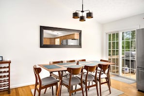A dining area with a wooden table and chairs, a large mirror, and a view of the kitchen and outdoor area. - Basye Bungalow | Spacious 4BR/3BA cabin with hot tub, fire pit, deck (Basye)