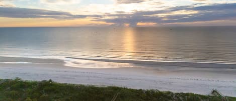 A beach with a clear sky, a calm sea, and a distant sunset.