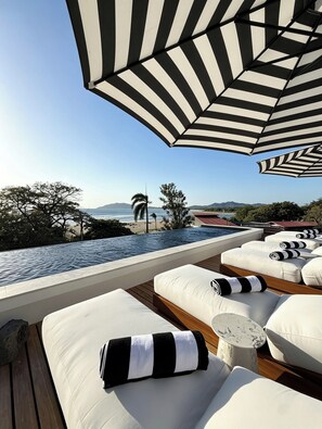 Eine Dachterrasse mit Pool, Liegestühlen und einem gestreiften Sonnenschirm.