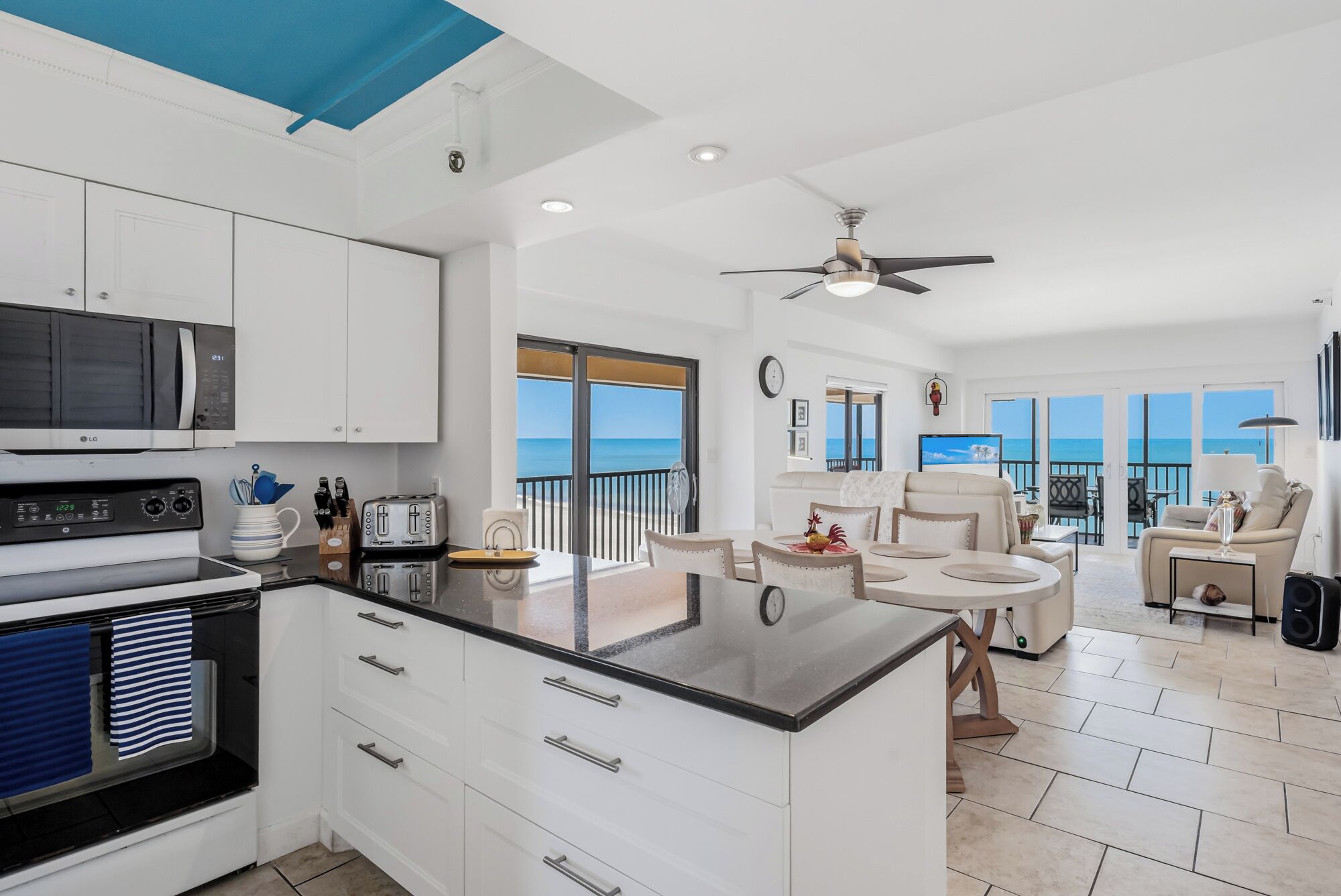 A modern kitchen with white cabinets, a microwave, and a stove. There is a balcony with a view of the ocean.
