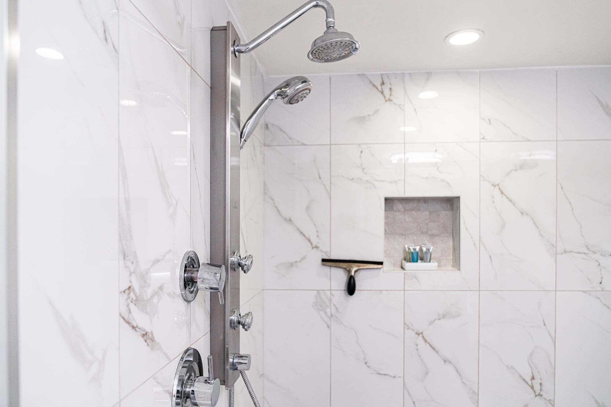Un baño moderno con ducha, baldosas de mármol y un pequeño estante con artículos de aseo.
