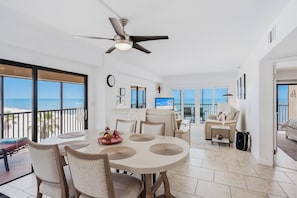 Ein geräumiges Zimmer mit Essbereich, Deckenventilator, Fernseher und einem Balkon mit Blick auf den Strand.