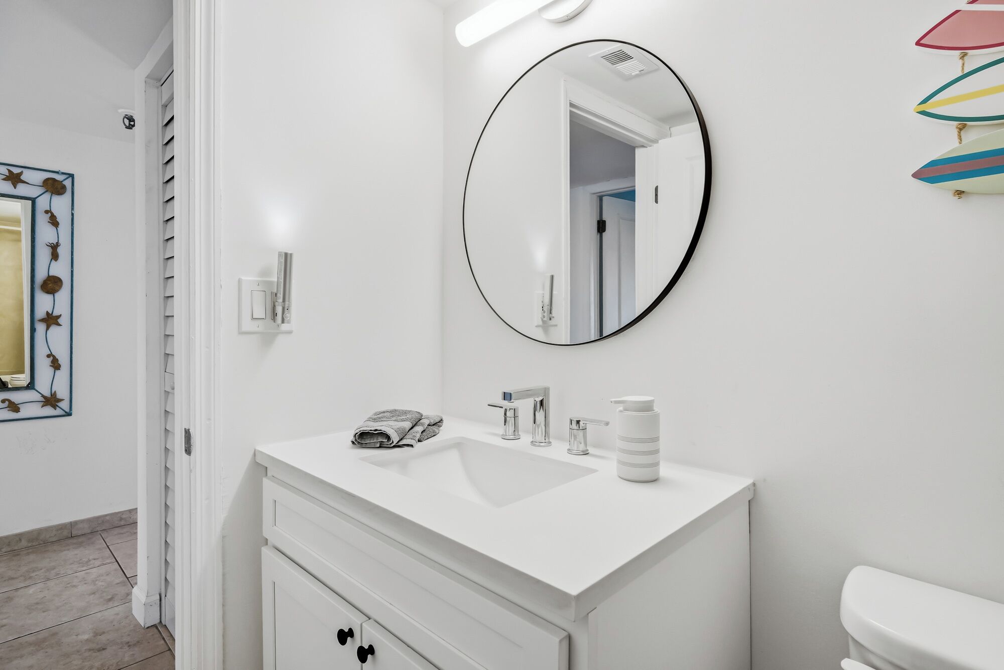 A modern bathroom with a white vanity, a round mirror, and a toilet.