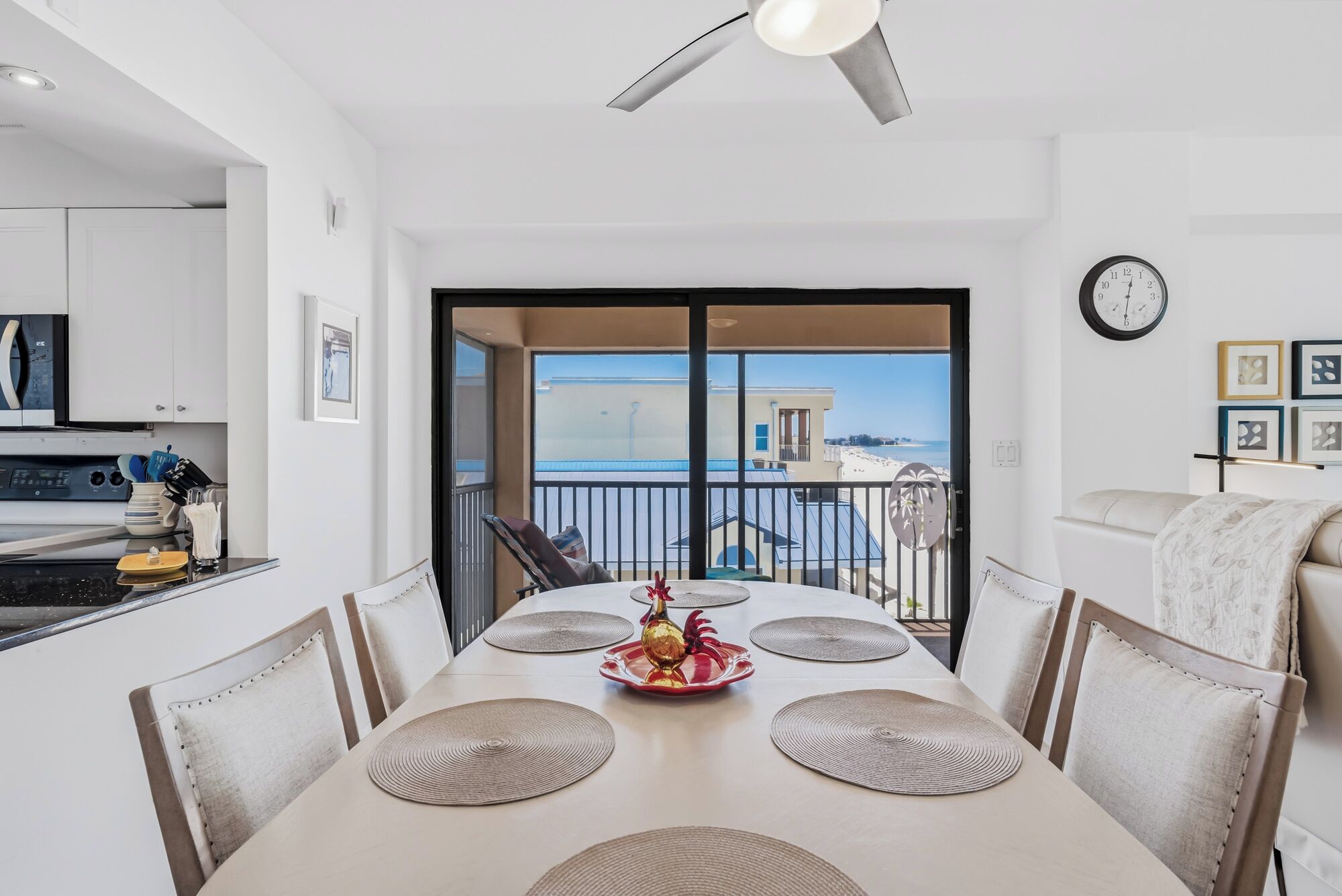 Comedor con una mesa dispuesta para cuatro, un ventilador de techo y vista al mar a través de un ventanal.