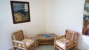 Une pièce comprenant deux fauteuils en osier, une petite table et un tableau encadré accroché au mur.