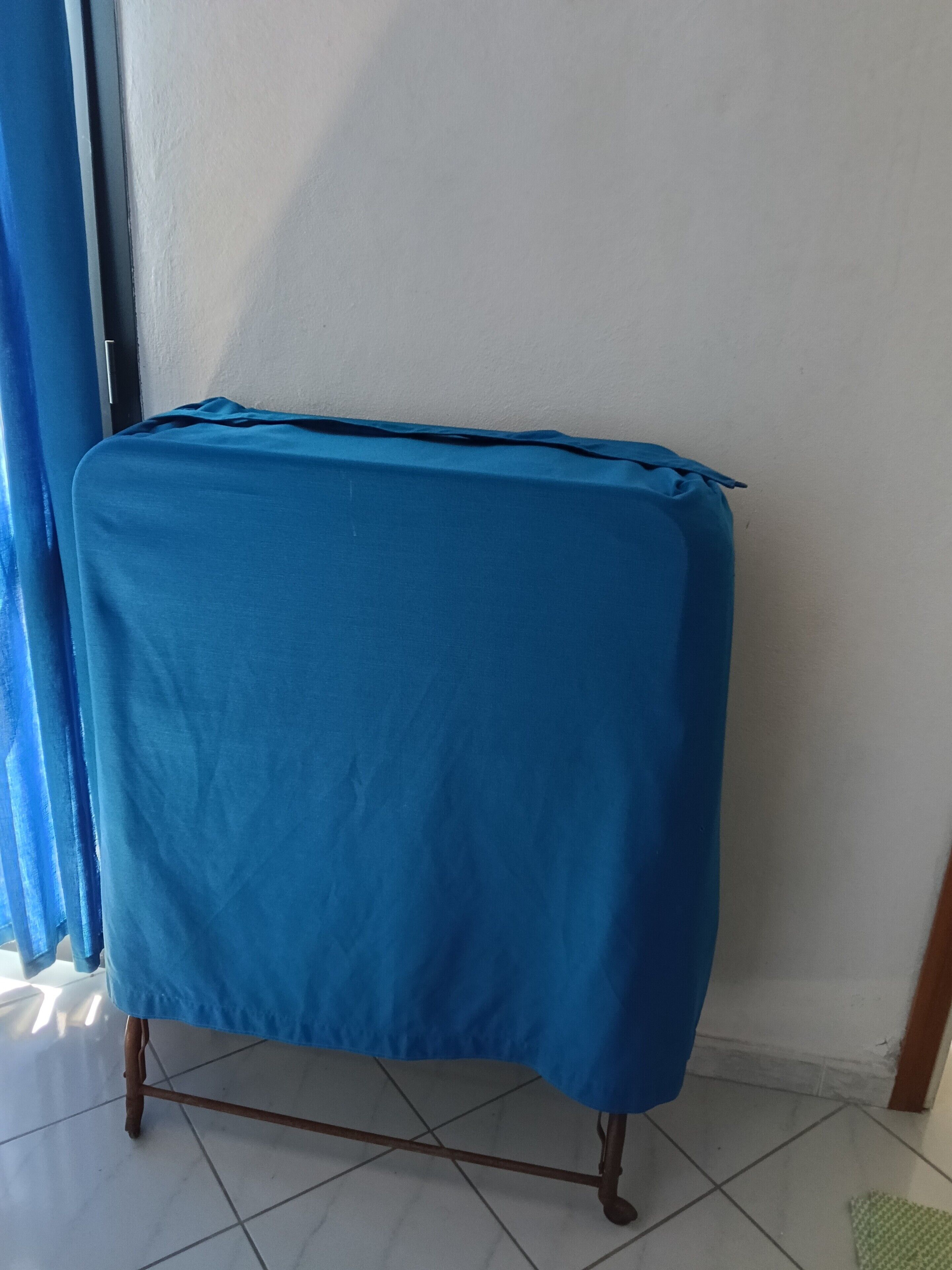 Une pièce avec une table recouverte d’une nappe bleue, un mur blanc et un sol carrelé.