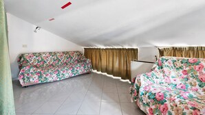 A room with two sofas covered in floral upholstery, a tiled floor, and a ceiling with recessed lighting.
