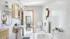 A bathroom with a bathtub, a shower, a sink, and a toilet. There is a towel rack, a mirror, and a shelf with toiletries.