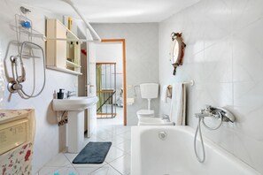 Ein Badezimmer mit Badewanne, Dusche, Waschbecken und Toilette. Ein Handtuchhalter, ein Spiegel und ein Ablagebereich mit Pflegeprodukten sind ebenfalls vorhanden.