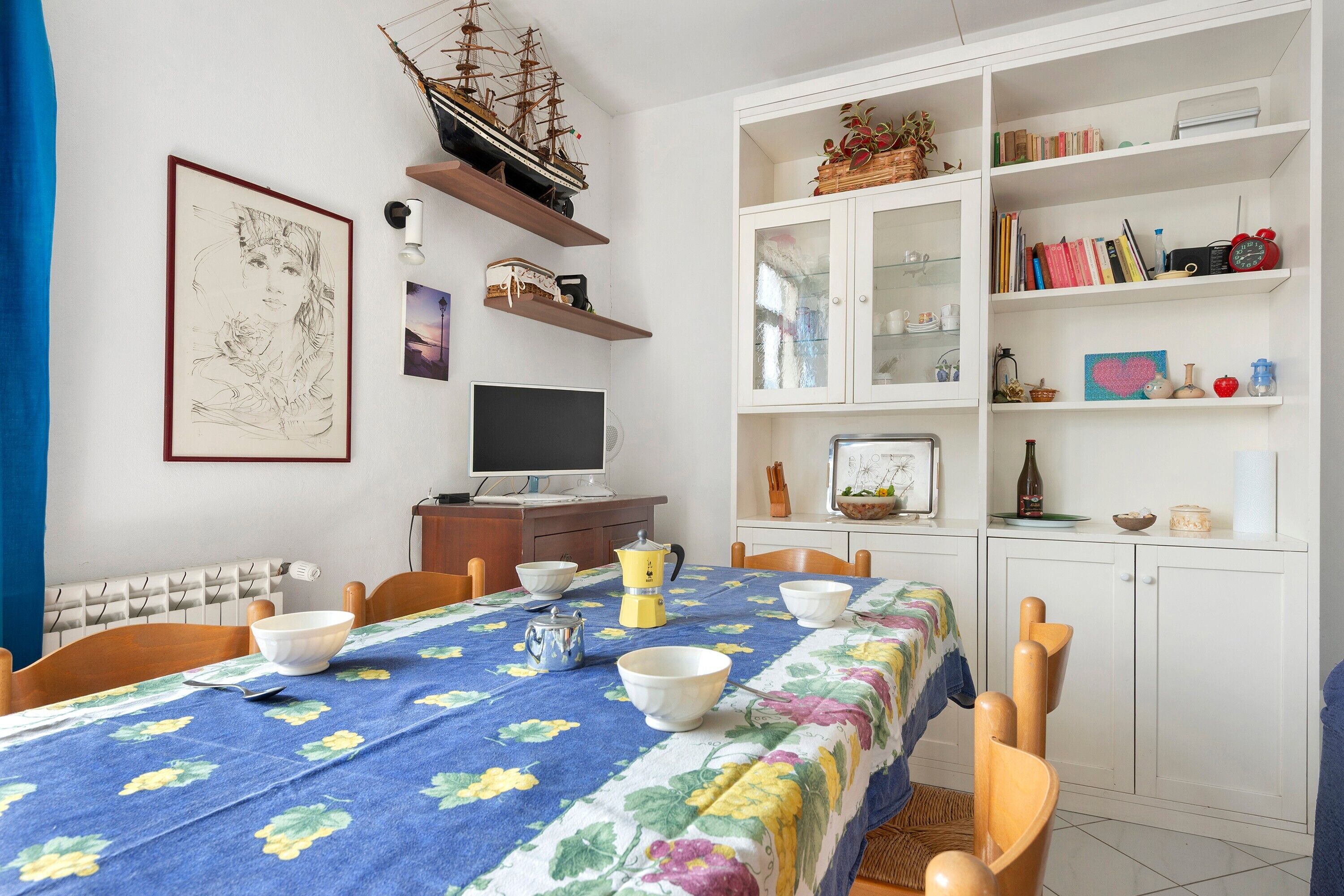 Un coin repas avec une table dressée pour quatre personnes, une maquette de bateau et une bibliothèque contenant divers objets.
