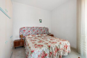 Un dormitorio con colcha estampada, mesitas de noche de madera y un pequeño aparador junto a la cama, además de un cuadro en la pared.