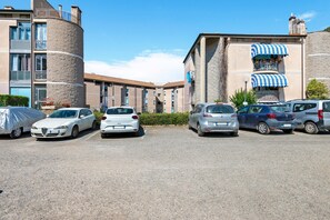 A parking lot with several cars, a building with a stone facade, and a blue-striped awning.