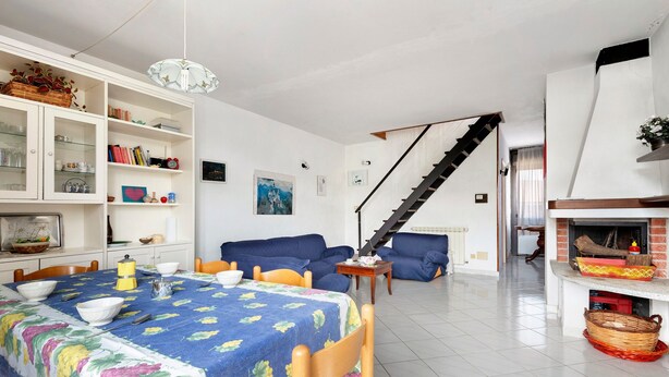 A living room with a dining table, sofas, a fireplace, and a staircase.