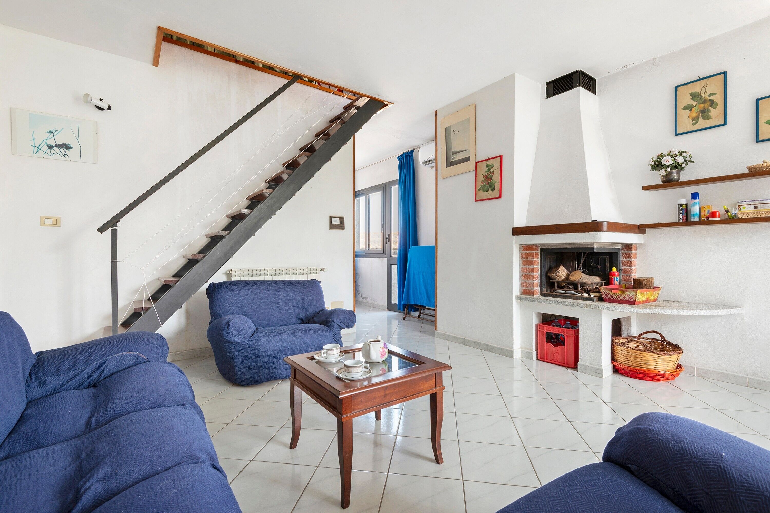 Ein Wohnzimmer mit Treppe, blauen Sofas, einem Couchtisch mit Teeservice und einem Kamin.