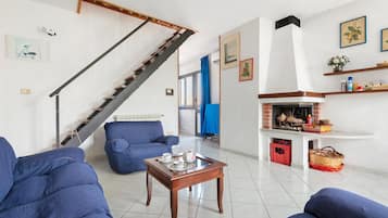 Ein Wohnzimmer mit Treppe, blauen Sofas, einem Couchtisch mit Teeservice und einem Kamin.