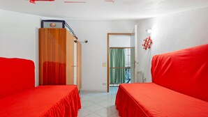 A room with two beds, a wooden wardrobe, a radiator, and a door leading to another room.