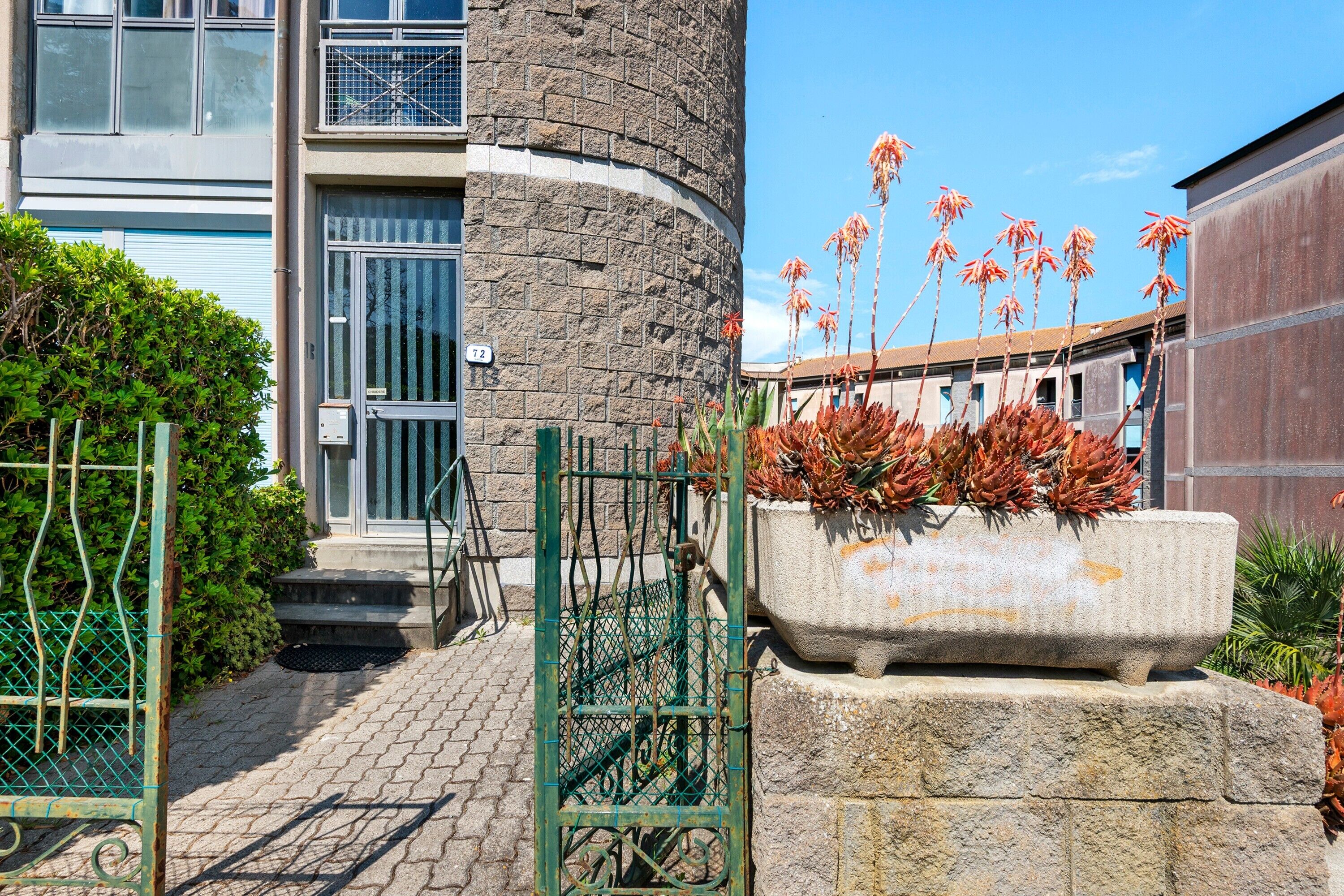 A building with a stone facade, a metal gate, and a planter with red flowers.