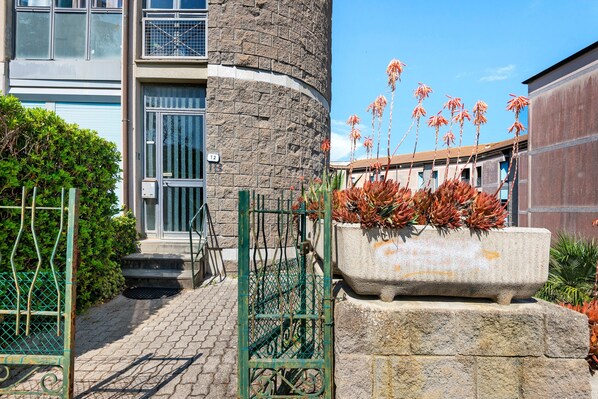 Un edificio con fachada de piedra, una reja metálica y una jardinera con flores rojas.