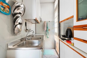 Una cocina con lavamanos de acero inoxidable, hervidor y microondas.