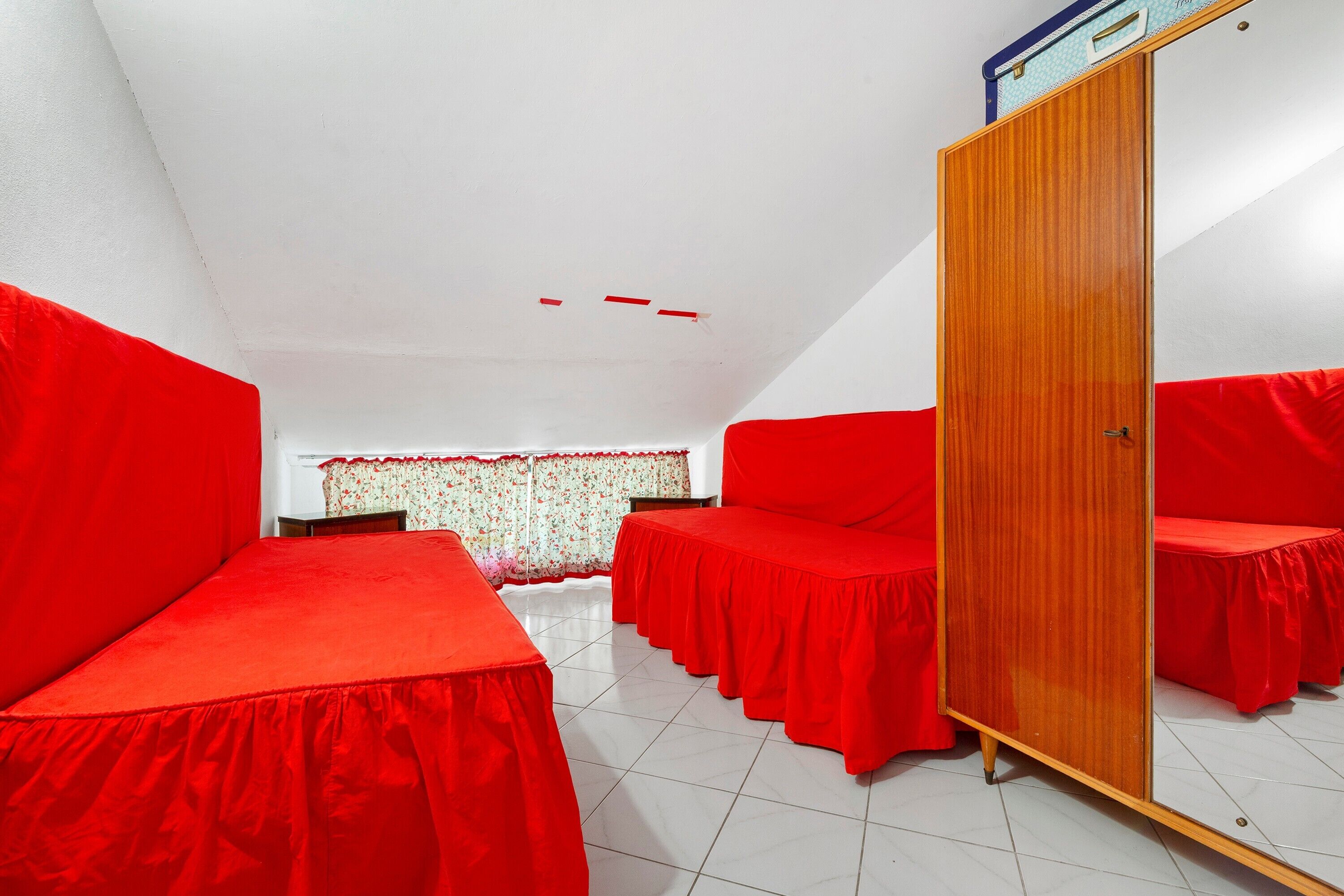 A room with red beds, a wooden wardrobe, and a tiled floor.