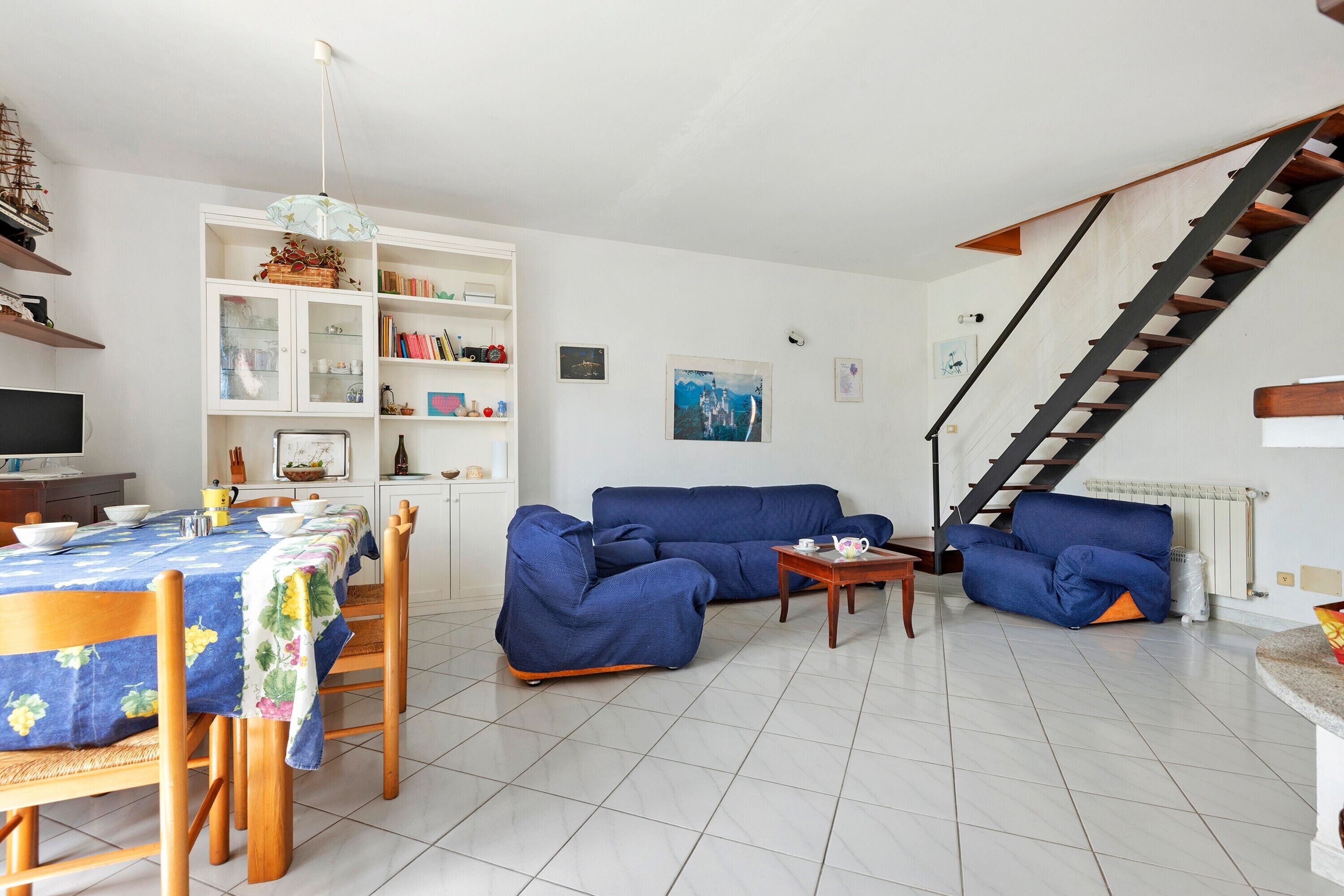 A living room with a sofa, dining table, and chairs, a staircase, and a bookshelf.