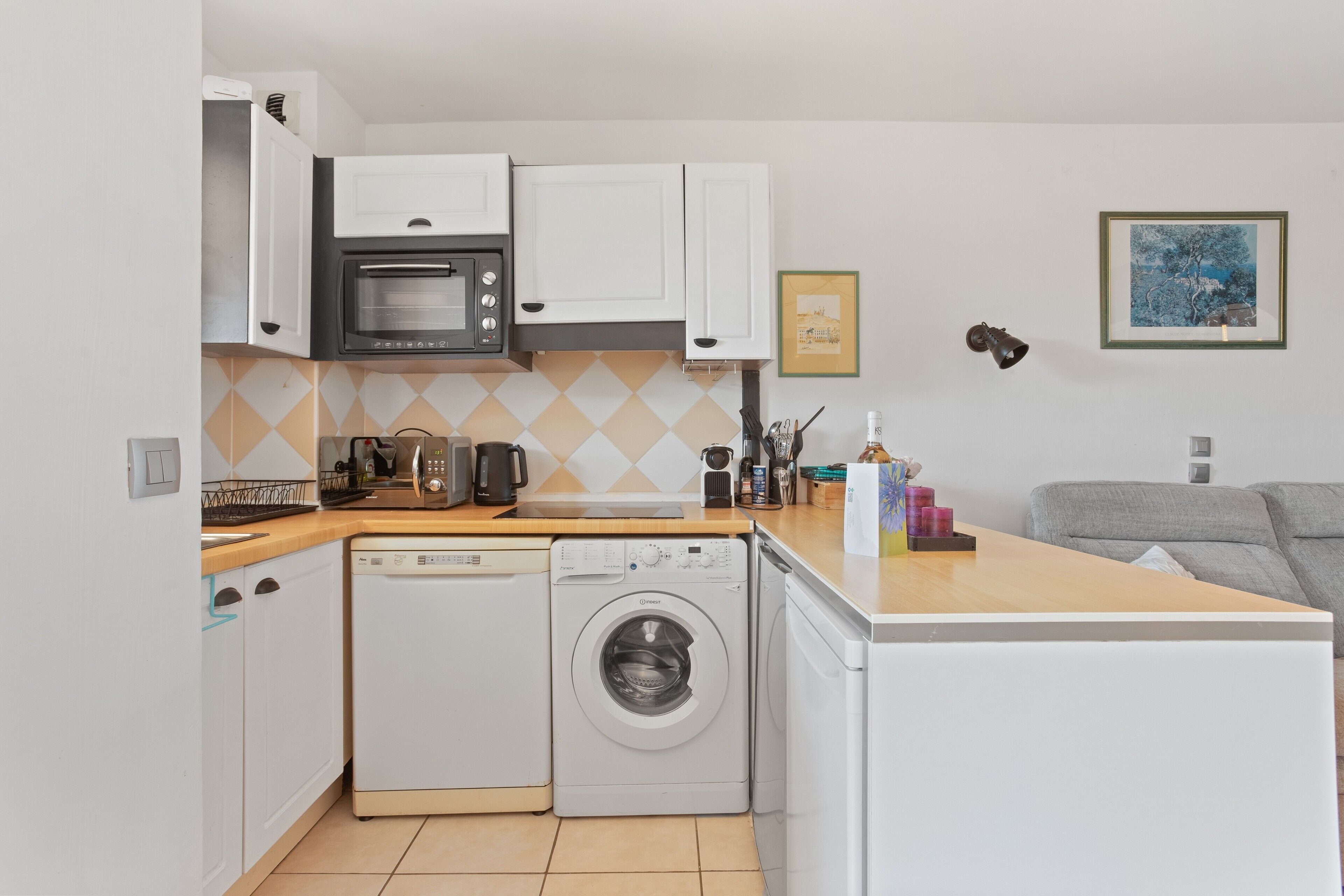 A compact kitchen with a microwave, oven, and washing machine, a small sink, and a countertop with various items.