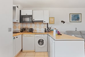 Cocina compacta con microondas, horno y lavadora, un lavamanos pequeño y una encimera con varios objetos.