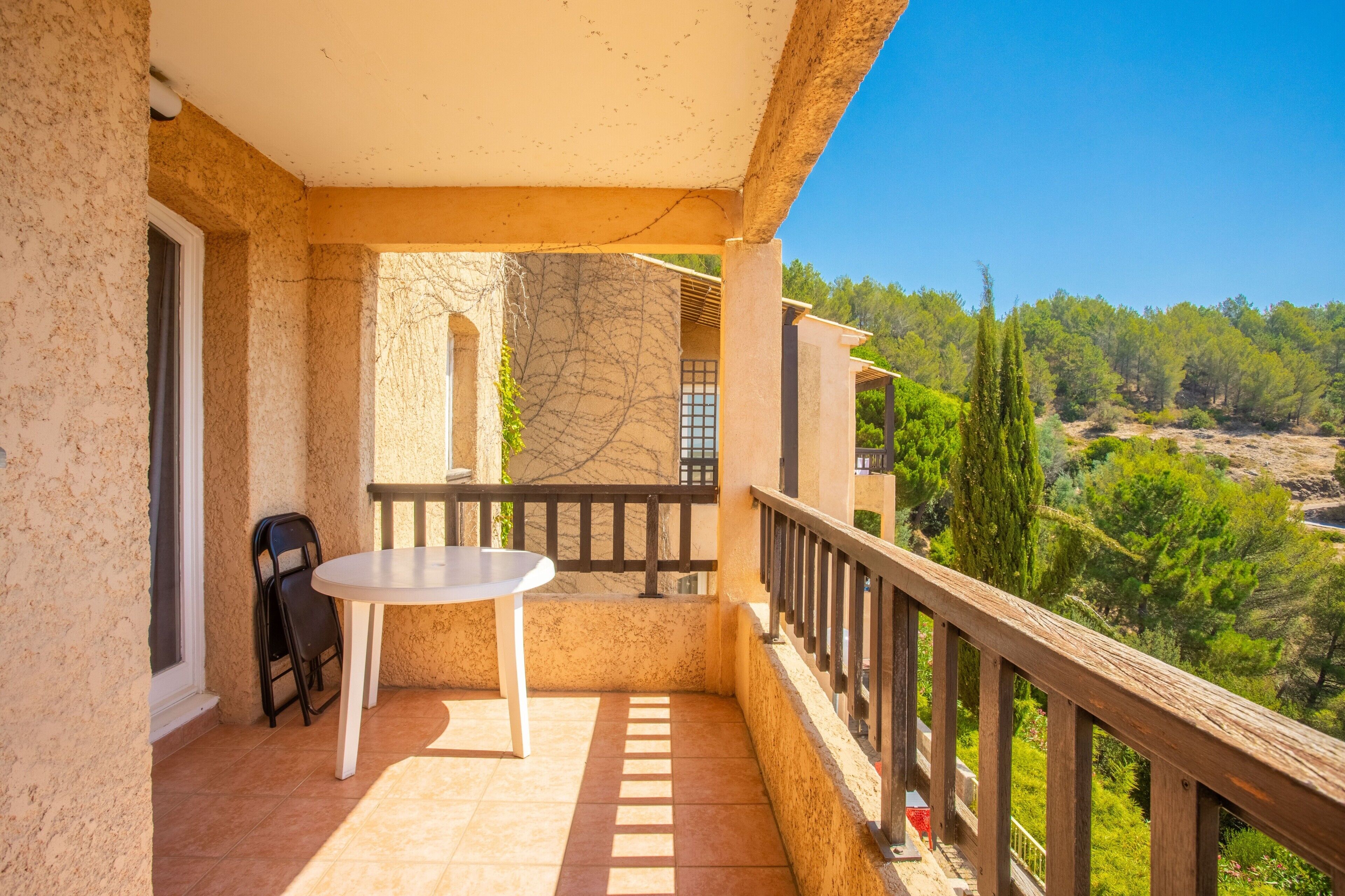 Un balcon avec une table et des chaises, une vue sur les arbres et les collines, et une balustrade en bois.