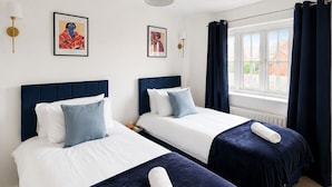 Quarto de hotel com duas camas, uma janela com cortinas, luminárias fixadas na parede e dois quadros emoldurados.