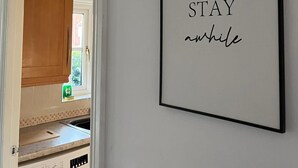 Um quadro com o texto 'STAY while' numa parede em um quarto com máquina de lavar e armários.