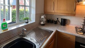 Cozinha com pia, armários de madeira, uma janela e vista para as casas lá fora.
